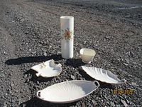 Five vintage Lenox china items displayed outdoors on gravel: floral vase, fleur de lis shield ashtray, two condiment dishes (one leaf-shaped and one with handles), and a small bowl.