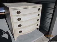 Full view of the solid mahogany chest painted in off-white with four drawers and brass handles.