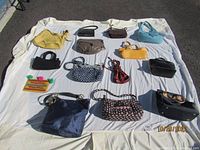 Image showing 15 assorted purses laid out on a white cloth, displaying variety in color, style, and size.