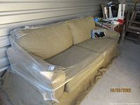 Green solid color sofa wrapped in clear plastic, with loose back and seat cushions visible, the sofa includes a skirted bottom and is in clean condition.