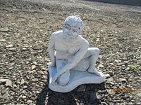 Front view of hand crafted man sitting on stone sculpture, showing detailed facial features and body.