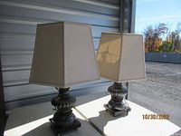 Pair of matching table lamps with square beige fabric shades and dark bases on a white surface with natural light.