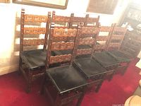 Front view of all eight chairs in a row showing carved backs and leather seats