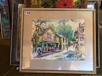 Full view of the framed watercolour painting showing street scene with buildings and walking figures.