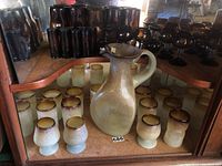 Overall display of pale green and brown-rimmed pitcher surrounded by matching glasses in display case