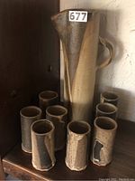 Full view of the pitcher and eight glasses arranged on a wooden surface, showing overall set composition and colors.