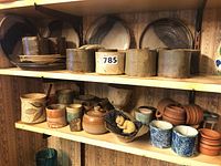 Shelf of various mid century modern pottery including plates, bowls, cups, containers, and a small ceramic dog figurine