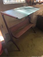 Left side view of teak cantilever table showing curved frame and lower shelf