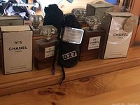 Photo displaying multiple bottles of Chanel No. 5 Eau De Parfum and one Geoffrey Beene Grey Flannel Eau de Toilette spray wrapped in black fabric pouch.
