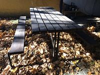 Full view of picnic table surrounded by fallen leaves, showing wooden slat top and bench seating with metal frame base.