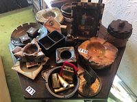 Overview of multiple vintage smoking accessories on table including ashtrays, lighters, trays and containers.