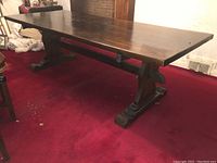 Full view of rectangular wood tabletop and one trestle pedestal base on red carpet.