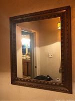 Full view of the rectangular mirror mounted on a wall showing the mirror glass and wooden carved frame.