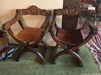 Front view of both chairs side by side showing carved wood frames and leather seats.