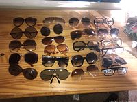 Wide view of 18 pairs of mixed vintage sunglasses arranged on wooden surface