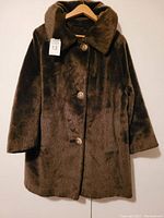 Full view of brown vintage style faux fur coat hanging on wooden hanger showing coat length and button front.