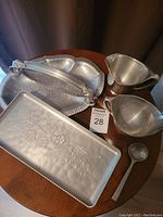 Photo of hand-wrought rectangular aluminum tray with floral embossing, creamer, sugar bowl and spoon on wood surface