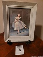 Photo of framed ballerina print featuring a ballerina in a white tutu with floral headpiece, seated on display stand
