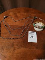 Photo of the cloisonne hinge bracelet, silver-tone chain, and MaxSold lot card on a wooden surface.