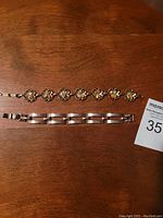 Two bracelets laid flat on wooden table, showing the stainless steel link bracelet and vintage gemstone bracelet with amber-colored stones.