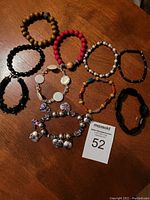 Photo of varied bracelets arranged in a circle on wooden surface, showing individual details including beads and metal charms.