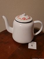 White enamel coffee pot with floral lid viewed from the side on a wooden table with lot tag