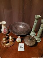 Photo of multiple home decor items including candlesticks, vases, brass salt and pepper shakers on a tray, a large decorative metal bowl, and a lidded metal container.
