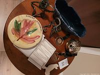 Photo of table with assorted items including maple leaf ceramic plate, blue flower container, metal candle holders, ceramic ashtray, medal, polar bear figurine, and glass cigarette holders