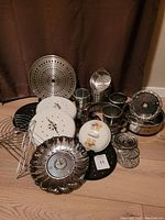 Overview of metal kitchenware lot on floor with multiple lids, trivets, steamers, and utensil holders displayed