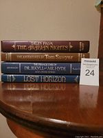 Stack of four hardcover books showing spines: Tales from The Arabian Nights, The Adventures of Tom Sawyer, Dr. Jekyll and Mr. Hyde and Other Stories, Lost Horizon
