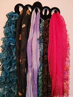 Close-up photo showing six scarves on the hanger with distinct colors and patterns including blue ruffles, black with floral pattern, lavender, teal, multi-colored, and pink.