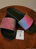 Pair of iridescent slide on flip flops with black soles and wide shiny straps showing color gradient and faint embossed patterns.
