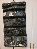 Large black hanging roll bag with multiple clear zippered compartments hanging vertically on white background