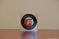 Front view of the signed 1972 Summit Series hockey puck in a clear display case showing Marcels Dionne's autograph and inscriptions