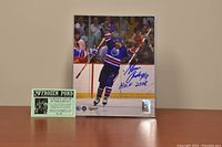 Signed 8x10 color photo of Glenn Anderson celebrating on ice in Edmonton Oilers blue jersey, with signature and Hall of Fame year inscription in blue ink on white border. Certificate of authenticity displayed to the left of photo.