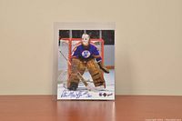 Signed 8x10 photo showing Peter McDuffe in vintage goalie uniform for Kansas City Scouts standing in front of the net.