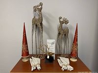 Photo of the full set showing two red cone-shaped Christmas tree decorations on wood bases, three tall gold glitter reindeer decorations of varying size, four white cloth napkins with gold and rhinestone napkin rings, and a white scent diffuser box with gold reindeer graphic.