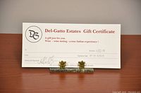 Photo of the $50 Del-Gatto Estates gift certificate on wooden surface held upright by a clear stand.