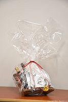 Wicker gift basket wrapped in cellophane with red ribbon showing mug, spices, olive oil, vinegar, coffee, bowl