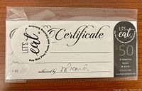 Photo showing a sealed plastic sleeve containing multiple $50 gift certificates from Hay Bay Fine Foods and Catering Services. The certificates include the business name, address, phone number, email, and authorized signature line.