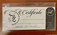 Photo of $75 gift certificate in clear plastic sleeve showing details, authorization, and branding.