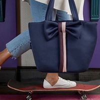 Navy handbag being held by a person standing on a skateboard, showing scale and carry style.