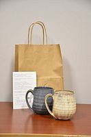 Photo showing two handcrafted mugs with artisan glazes and a paper bag with The Ye11ow Studio branding.