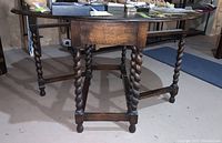 Full view of antique wooden gateleg table with barley twist legs and partially extended leaves, showing scratches and aged wood finish.