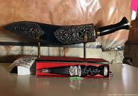Ceremonial kukri knife sheathed and displayed on metal stand with skean dhu dagger in tartan box in front.