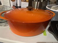 Orange enamelled cast iron Dutch oven with lid, showing front and one handle.