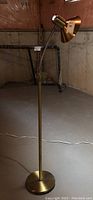 Full view of the gold tinted metal floor lamp showing the entire lamp from base to top, set in a basement environment.