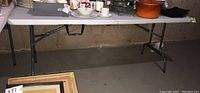 Full view of the white resin folding table showing metal legs and the tabletop loaded with various items.