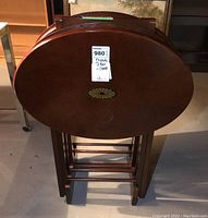 Photo showing all four oval wooden TV folding tables stacked and stored in a wooden stand, highlighting the overall design and arrangement.