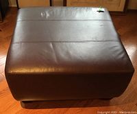 Top view of large brown leather ottoman with horizontal stitching and slight indentations.